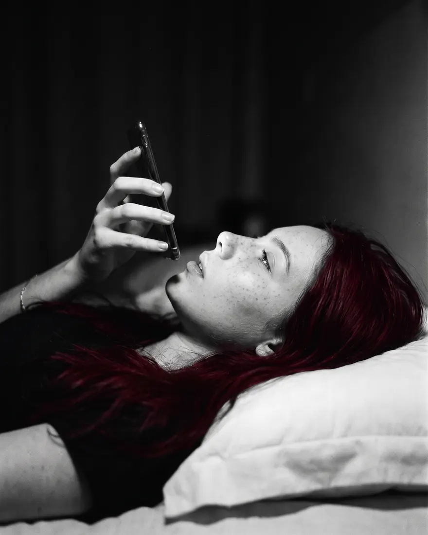 A mesma mulher deitada no escuro, perto da meia-noite, mandando um áudio pelo celular.